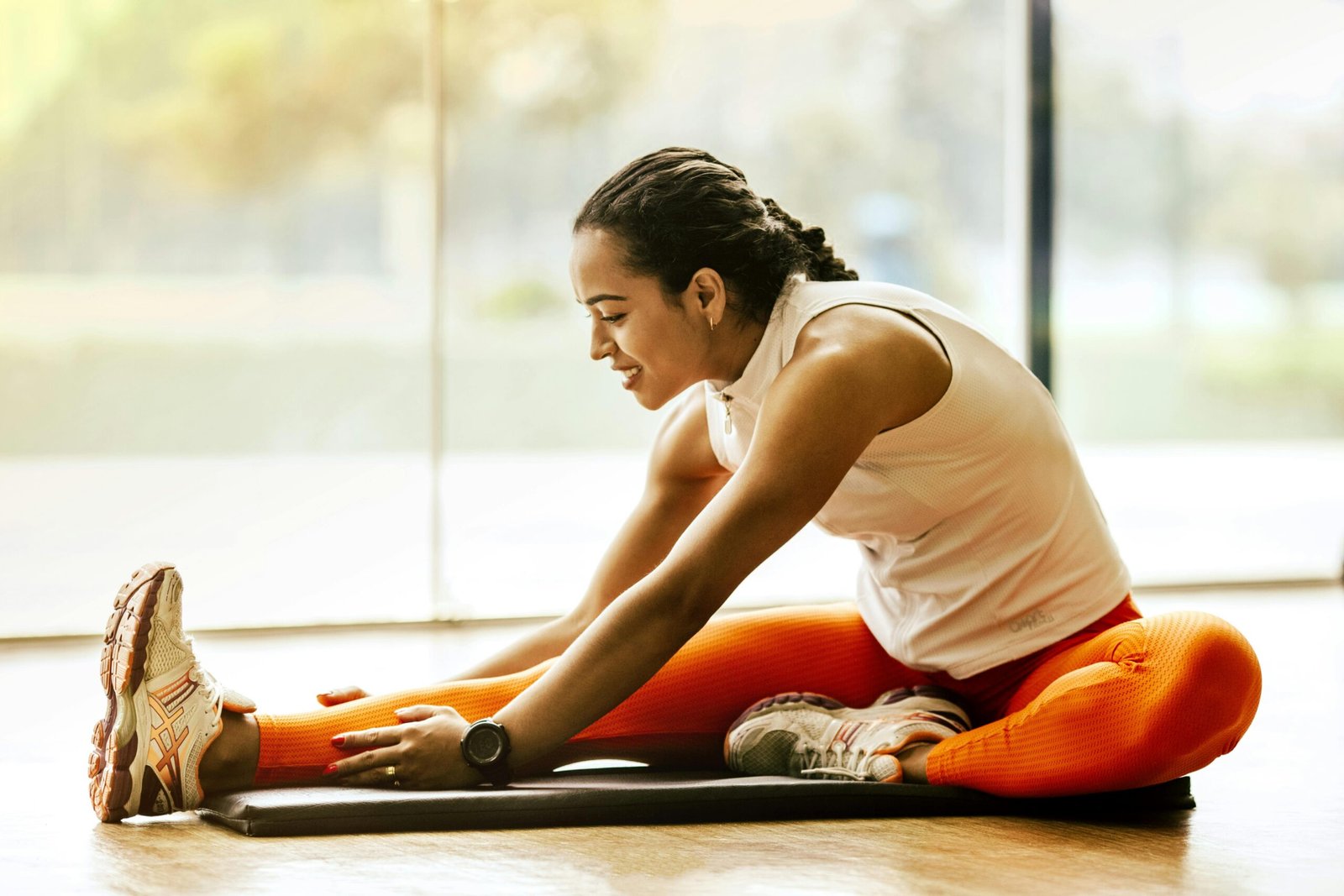 A young girl is engaged in a fitness routine, stretching her arms while standing on a mat. She appears focused, wearing athletic clothing, with a bright, spacious room in the background.